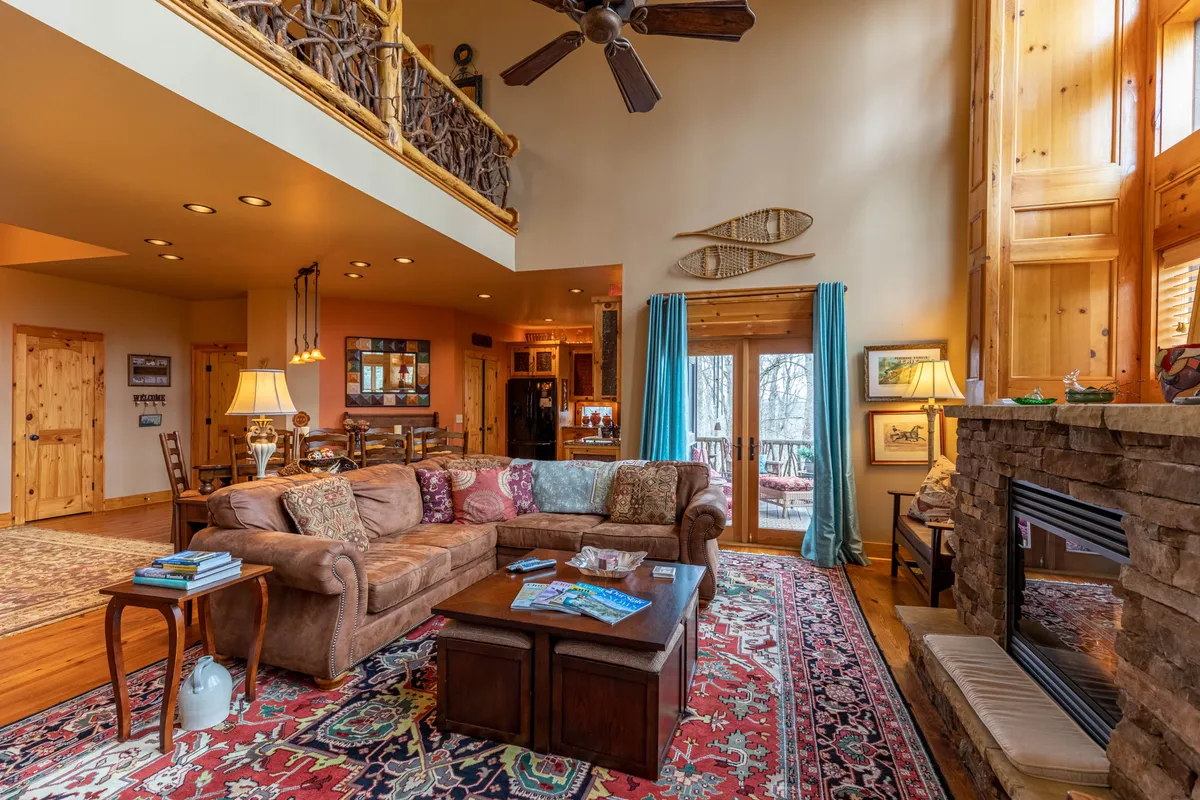 The living area boasts a comfortable brown sofa, a crackling fireplace, large windows letting in natural light, and decorative oars on the wall, reinforcing the home's connection to outdoor activities. The colorful area rug adds a cozy touch.