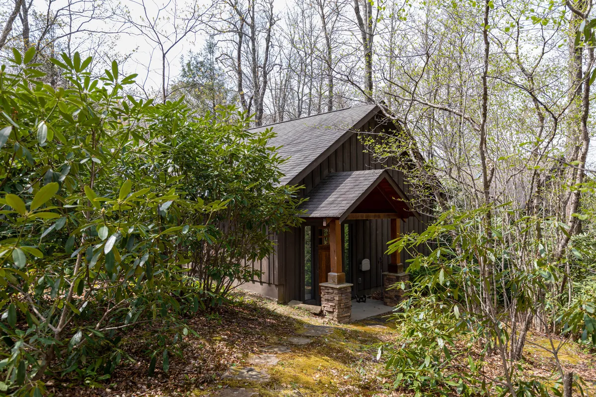 This image features the cabin's inviting entrance, surrounded by lush greenery and approached by rustic stone steps. The peaceful natural setting suggests easy access to outdoor adventures and immersion in the landscape.