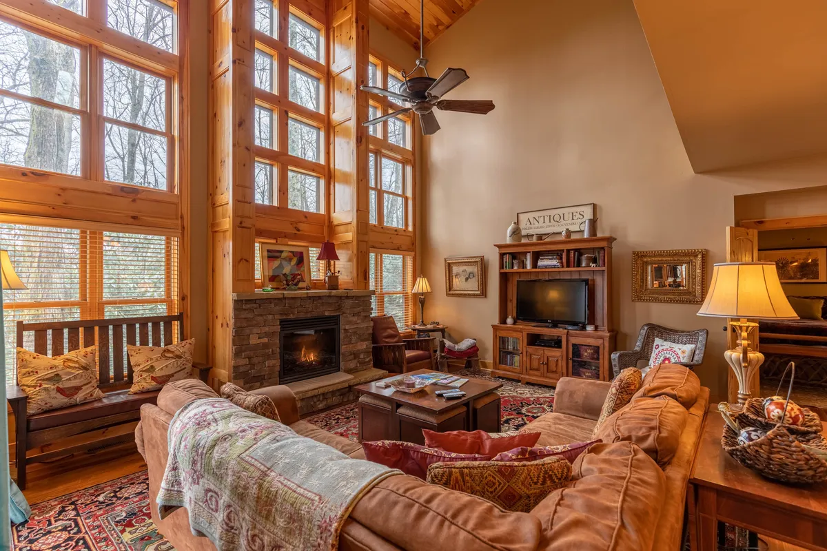This interior image shows a spacious living room with large windows, a cozy fireplace, comfortable seating, and decorative accents. The scene is warm and welcoming, ideal for socializing, relaxing, or enjoying movie and game nights as a family.