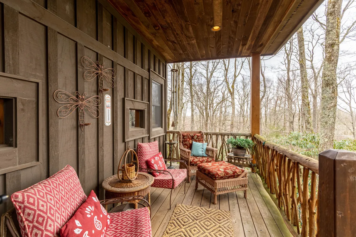 The scene features a wooden deck with a natural wood railing, decorative pillows, and a woven rug. Surrounded by lush trees and foliage, the deck offers a feeling of immersion in nature. The space is styled for relaxation and taking in views of the High Country.
