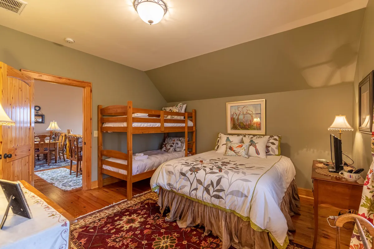 A spacious family bedroom with a queen bed adorned with floral bedding and a set of bunk beds. Wood furniture and soft lighting create a warm, family-friendly environment ideal for both adults and children.