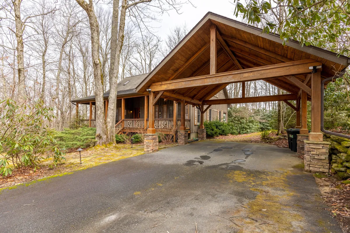 The exterior view of the home's wooden structure with stone accents, surrounded by dense greenery. The driveway is visible, suggesting convenient paved parking and easy access for all ages.