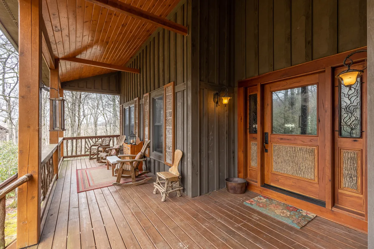 This exterior image features a cozy wooden entrance door, rocking chairs set on the porch, a decorative rug, and warm light fixtures. The scene exudes comfort and hospitality, hinting at leisurely mornings or evenings on the porch.