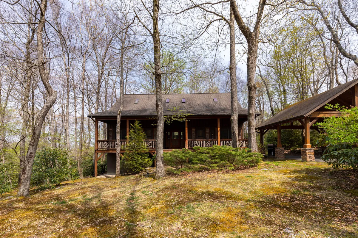 This exterior image showcases a welcoming wooden porch surrounded by tall trees, stone accents, and lush green foliage. The porch invites relaxation and gatherings while the natural setting suggests proximity to nature and local attractions.
